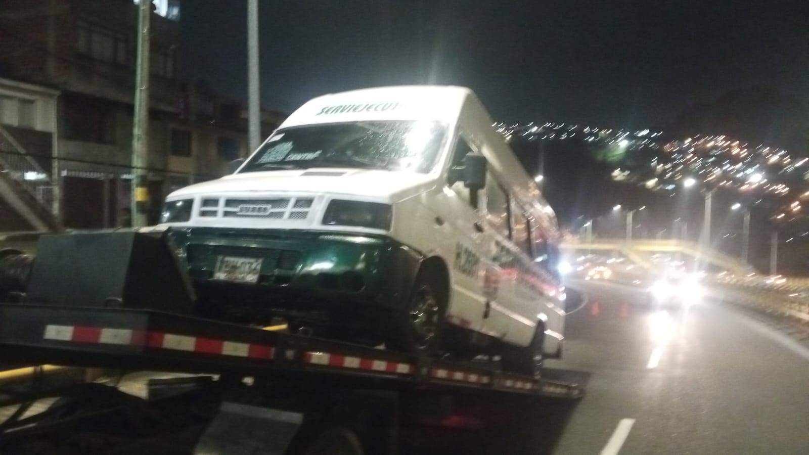 Servicio nocturno de grúa remolcando minibús en vía urbana